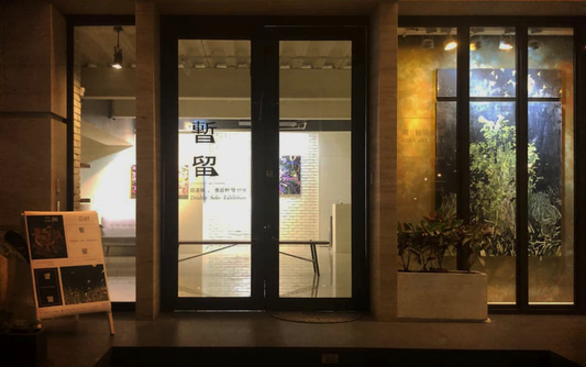 Entrance view of Dao Ming Chuang's Stay Temporarily exhibition, showcasing the gallery's glass doors with illuminated artworks visible inside.