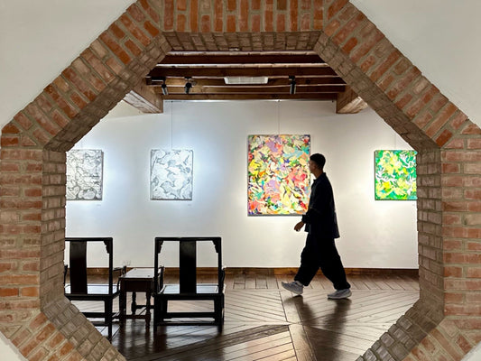 View of the Floating Shadows on the Blooming Path exhibition seen through a brick archway, with abstract paintings displayed on the far wall and a visitor walking through the gallery.